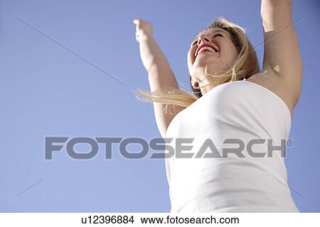 Young woman cheering with arms raised in front of blue sky, view from below View Large Photo Image Picture - Young woman cheering with arms raised in front of blue sky, view from below. Fotosearch