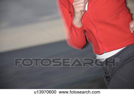 Stock Image - Upper part of woman's body jogging at the beach, side view. Fotosearch