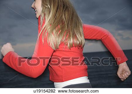 Stock Image - Upper part of woman's body jogging at the beach, side view. Fotosearch