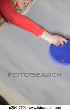 Stock Image - Woman playing with a frisbee, throwing and catching, in front of dark clouds. Fotosearch