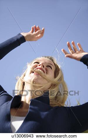 Stock Image - Young blond woman dancing, jumping and cheering at the beach, worm's eye view. Fotosearch