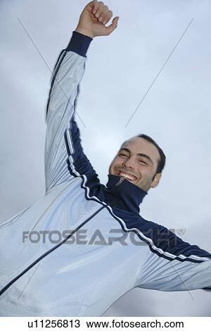 Stock Image - Young man in a sweat suit jacket cheering in front of dark clouds. Fotosearch