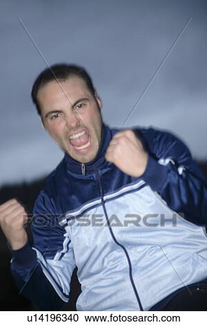 Stock Image - Young man in a sweat suit jacket cheering in front of dark clouds. Fotosearch
