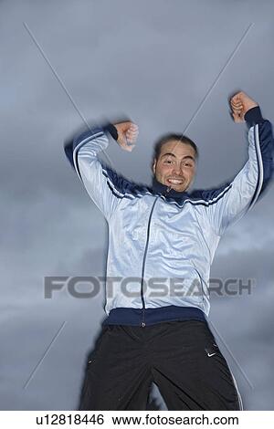 Stock Photograph - Young man in a sweat suit jacket cheering in front of dark clouds. Fotosearch