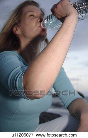 Young woman drinking mineral water from bottle at the beach at dusk View Large Photo Image Stock Photo - Young woman drinking mineral water from bottle at the beach at dusk. Fotosearch