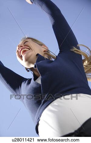 Young woman jumping happily in front of blue sky, view from below View Large Photo Image Stock Image - Young woman jumping happily in front of blue sky, view from below. Fotosearch