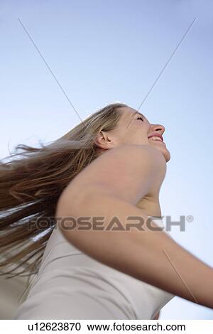 Stock Image - Young woman with long blond hair running at the beach, worm's eye view. Fotosearch