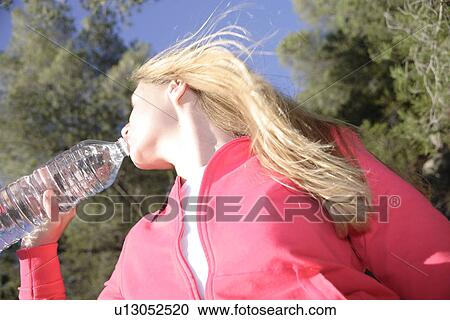 Stock Image - Female jogger drinking from water bottle, side view. Fotosearch