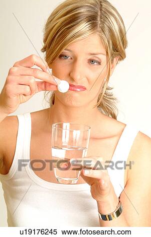 Stock Photography - Woman dropping fizzy tablet into glass of water, unhappy. Fotosearch