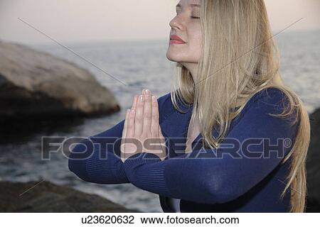 Stock Image - Woman on a rocky sea coast, meditating cross-legged, side view. Fotosearch