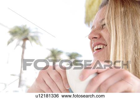 Stock Photograph - Young blond woman drinking cappuccino in a cafe, side view. Fotosearch