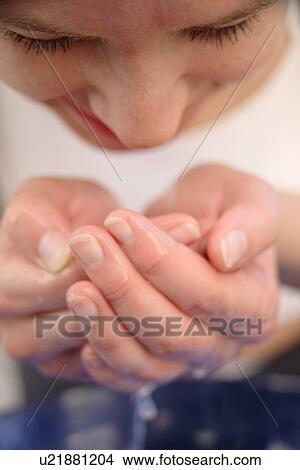 Picture - Young woman drinking water from her hands, close up. Fotosearch
