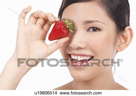 Portrait of Natural Young girl holding Strawberry in front of her eye View Large Photo Image Picture - Portrait of Natural Young girl holding Strawberry in front of her eye. Fotosearch