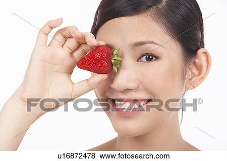 Portrait of Natural Young girl holding Strawberry in front of her eye View Large Photo Image Stock Photo - Portrait of Natural Young girl holding Strawberry in front of her eye. Fotosearch