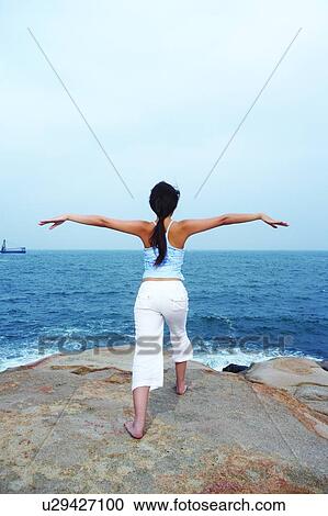 Stock Image - Young woman doing yoga, facing the sea. Fotosearch