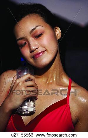 Stock Image - Young woman in sporty wear, standing near the sea, front view, close up, eyes closed. Fotosearch