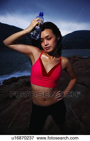 Stock Photo - Young woman in sporty wear, standing near the sea, front view. Fotosearch