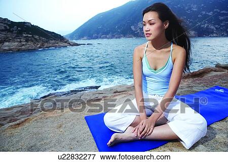 Stock Photo - Young woman sitting on exercise mat, smiling. Fotosearch