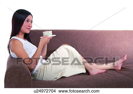 Picture - Young woman sitting on sofa, holding cup. Fotosearch