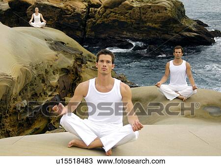 Stock Image - Two young men and a young woman practicing yoga. Fotosearch