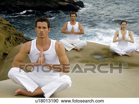 Stock Image - Two young men and a young woman practicing yoga. Fotosearch