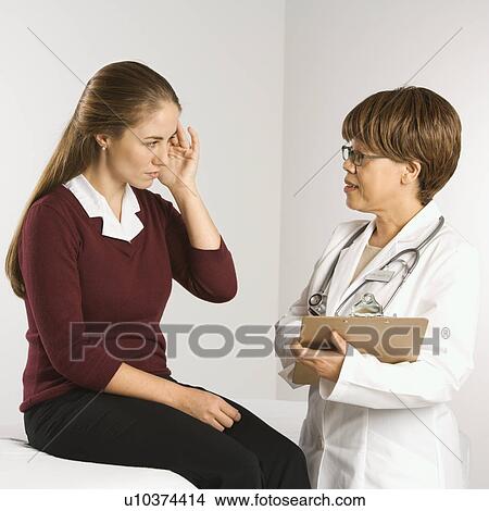 Picture - African American middle-aged female doctor listening to Caucasian mid-adult female patient explain her symptoms.. Fotosearch