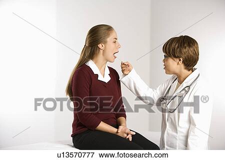 African American middle-aged female doctor examining Caucasian mid-adult female patient with tongue depressor. View Large Photo Image Stock Photo - African American middle-aged female doctor examining Caucasian mid-adult female patient with tongue depressor.. Fotosearch