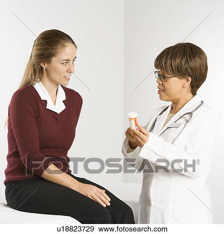 Stock Photo - African American middle-aged female doctor explaining medication to Caucasian mid-adult female patient.. Fotosearch