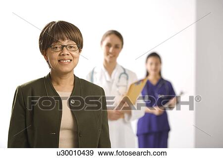 African American middle-aged woman smiling and looking at viewer with Caucasian mid-adult female doctor and Asian Chinese mid-adult female physician's assistant standing in background. View Large Photo Image Stock Photo - African American middle-aged woman smiling and looking at viewer with Caucasian mid-adult female doctor and Asian Chinese mid-adult female physician's assistant standing in background.. Fotosearch