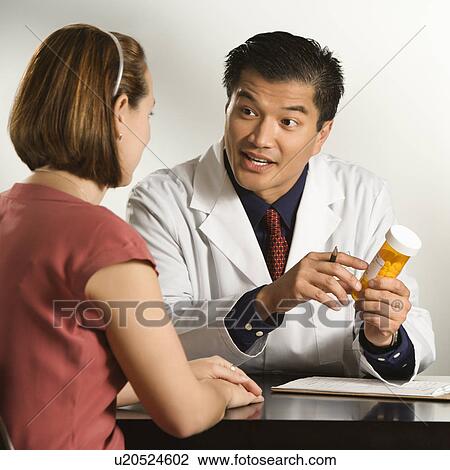 Stock Image - Asian American male doctor explaining medication to Caucasian female patient.. Fotosearch