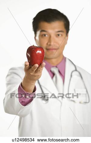 Asian American male doctor holding out apple. View Large Photo Image Picture - Asian American male doctor holding out apple.. Fotosearch