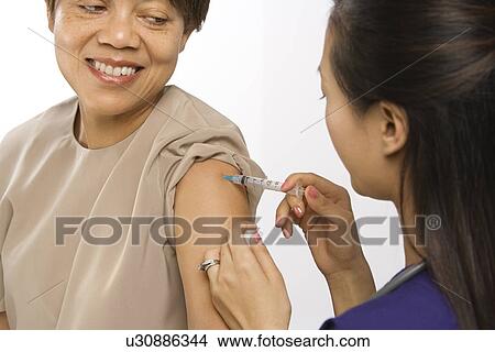 Asian Chinese mid-adult female medical practitioner giving shot in arm of African American middle-aged female patient. View Large Photo Image Picture - Asian Chinese mid-adult female medical practitioner giving shot in arm of African American middle-aged female patient.. Fotosearch