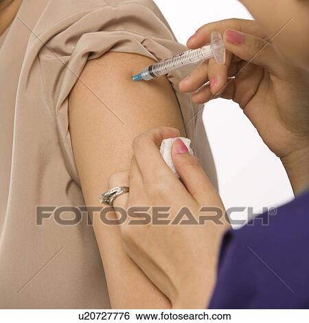 Stock Photograph - Asian Chinese mid-adult female medical practitioner giving shot in arm of African American middle-aged female patient.. Fotosearch