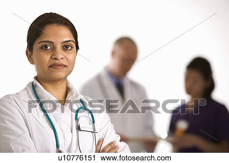Stock Image - Indian mid adult woman doctor standing with medical staff in background.. Fotosearch