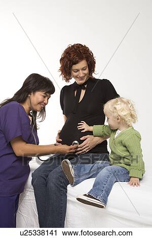 Stock Image - Nurse holding stethoscope on Caucasian pregnant woman's belly.. Fotosearch