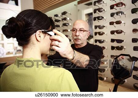 Stock Image - Optometrist adjusting glasses for woman in a store. Fotosearch