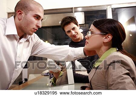 Stock Photography - Optometrist adjusting glasses for woman in a store. Fotosearch