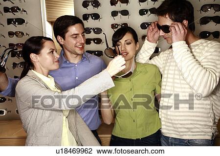 Stock Image - Two couples shopping for sunglasses in store. Fotosearch