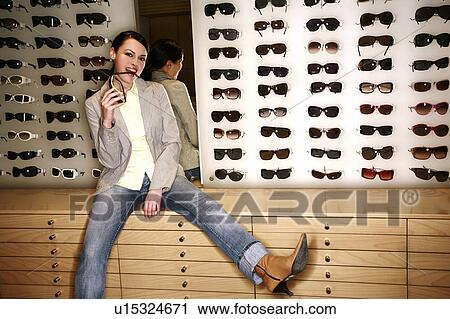Stock Image - Woman posing in front of sunglasses display. Fotosearch