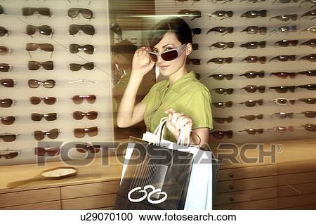 Stock Image - Woman shopping in sunglasses store. Fotosearch