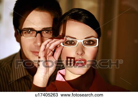 Woman wearing eyeglasses with optical exam characters on her face and man behind View Large Photo Image Stock Image - Woman wearing eyeglasses with optical exam characters on her face and man behind. Fotosearch