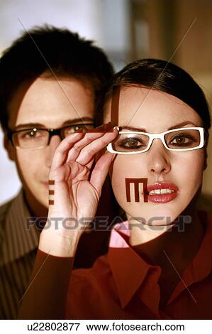 Stock Photo - Woman wearing eyeglasses with optical exam characters on her face and man behind. Fotosearch