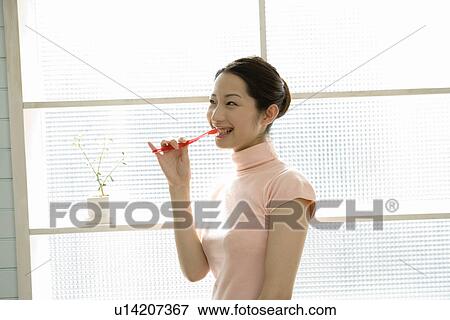 Stock Photo - A woman brushing teeth, side view, waist up. Fotosearch