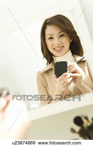Stock Photo - A woman holding a powder compact, reflected in the mirror, front view, white background, differential focus. Fotosearch