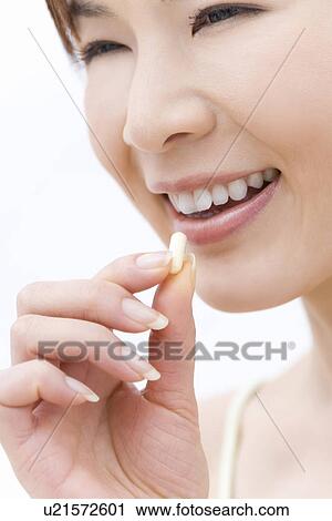 Stock Image - Close up of young woman taking a supplement, side view. Fotosearch