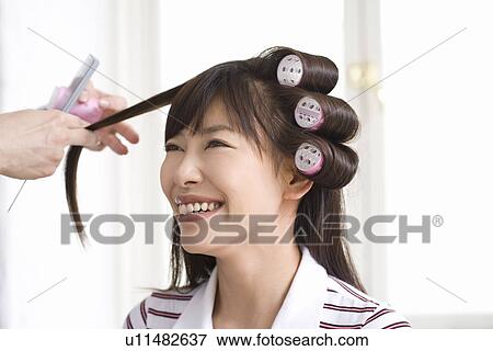 Stock Photo - Hairdresser cutting putting curlers in young woman's hair . Fotosearch