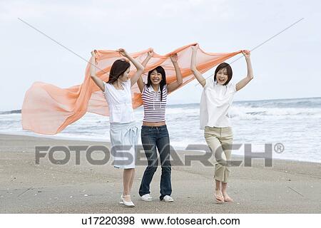 Three young women at beach, holding a shawl in the air, side view View Large Photo Image Stock Photo - Three young women at beach, holding a shawl in the air, side view. Fotosearch