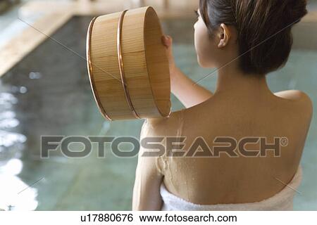 Stock Photograph - Woman pouring water on her shoulder with wooden tub, rear view, Japan. Fotosearch
