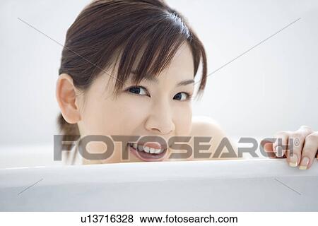 Stock Photo - Young woman in a bathtub, smiling, close up, front view. Fotosearch