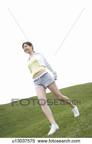 Stock Photography - Young Woman walking on lawn, low angle view. Fotosearch